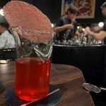 red drink in a beaker with a pink wafer balanced on top