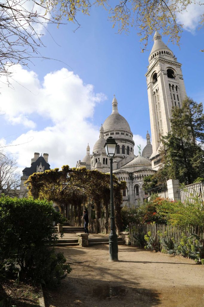 view of the bell tower and domes of sacre-coeur in Paris, from a park with arched walkway